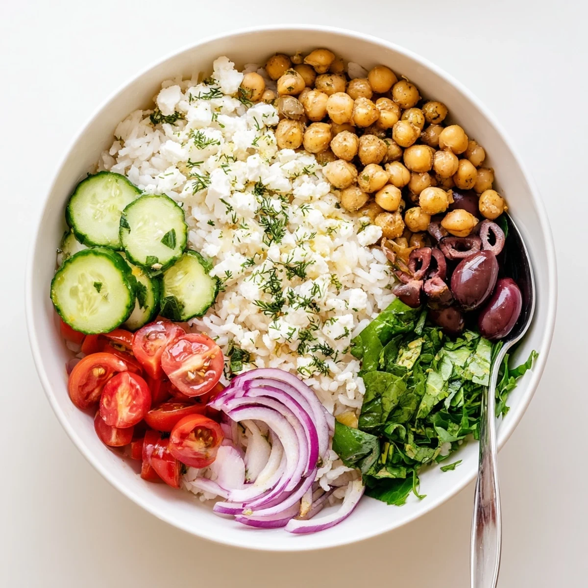 Colorful Mediterranean rice bowl topped with crisp vegetables, tangy feta, and fresh herbs