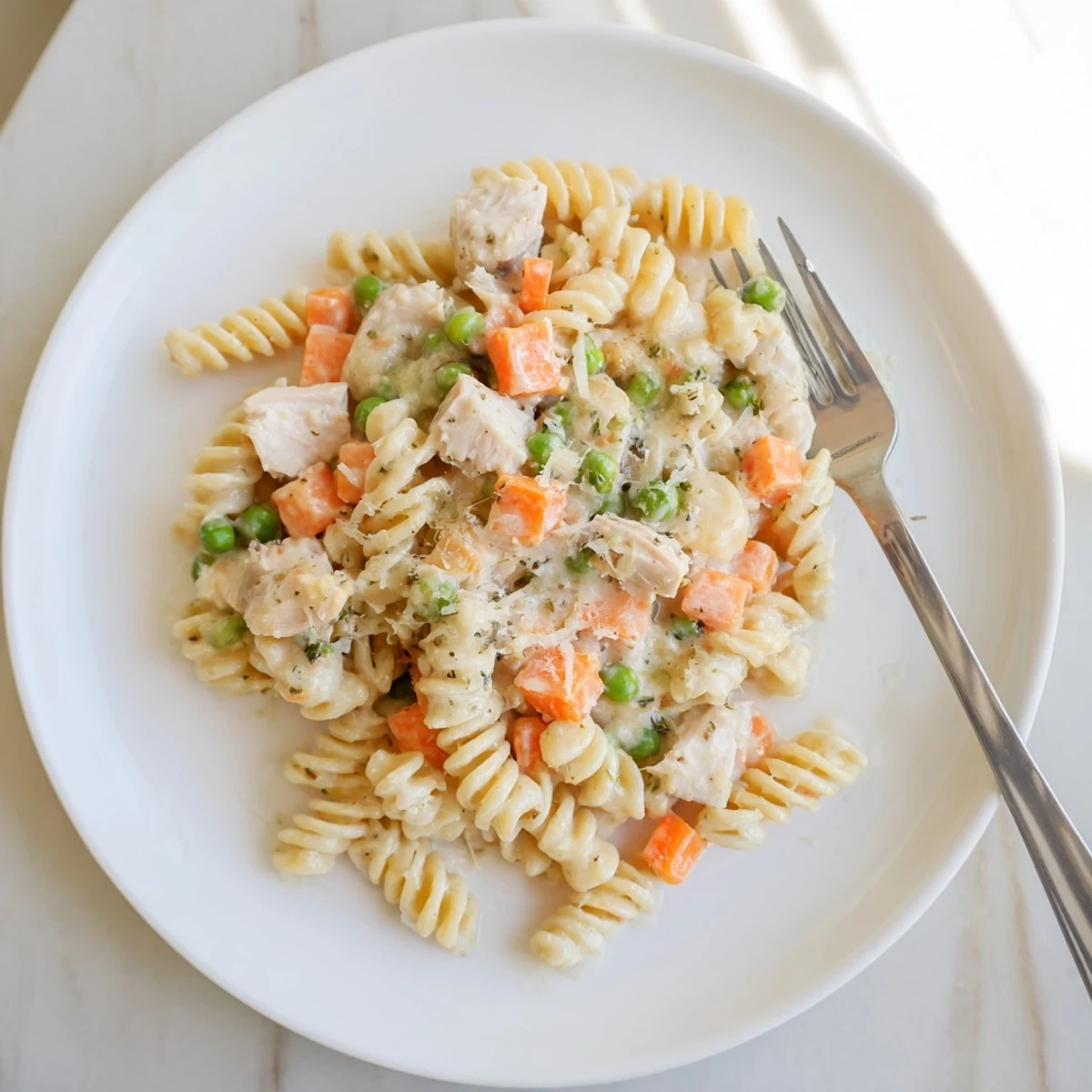 Hearty chicken pot pie pasta served in a bowl with colorful peas, carrots, and melted Parmesan