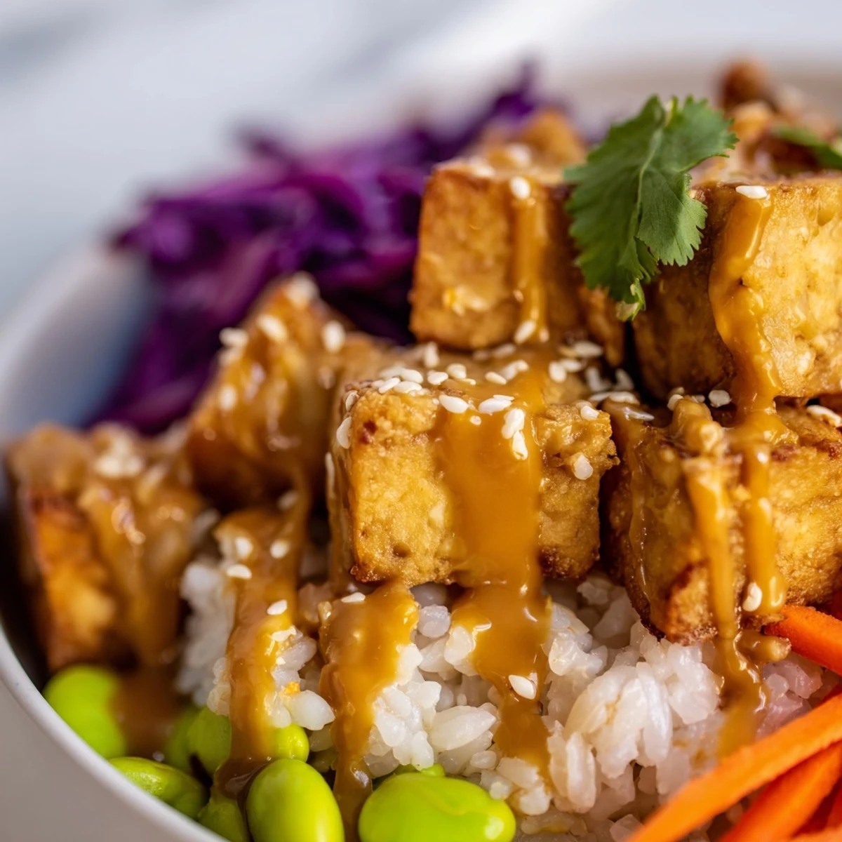 Tofu rice bowl with peanut sauce topped with colorful julienned vegetables and sesame seeds