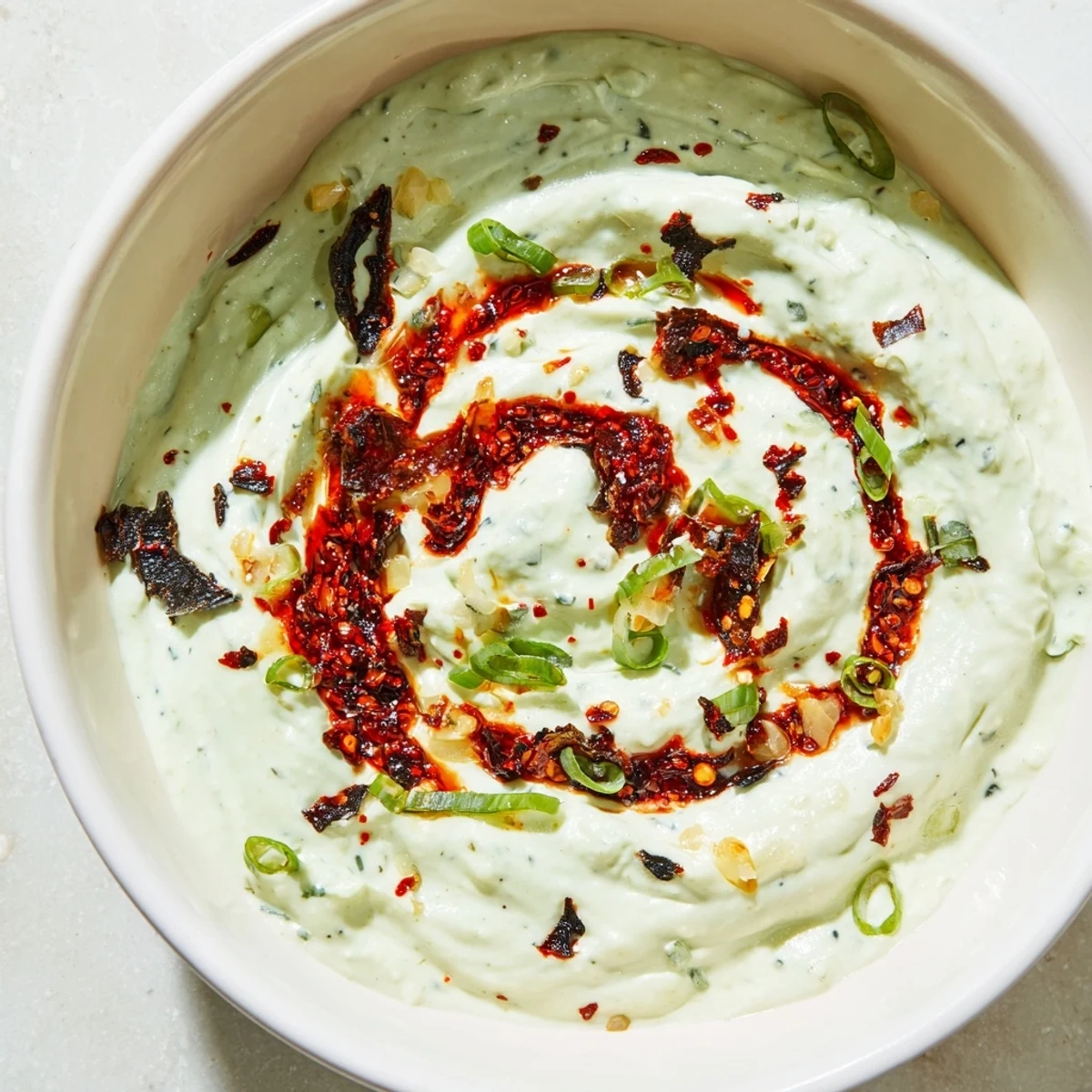 Creamy charred scallion and chili crisp dip swirled with spicy oil in a rustic bowl