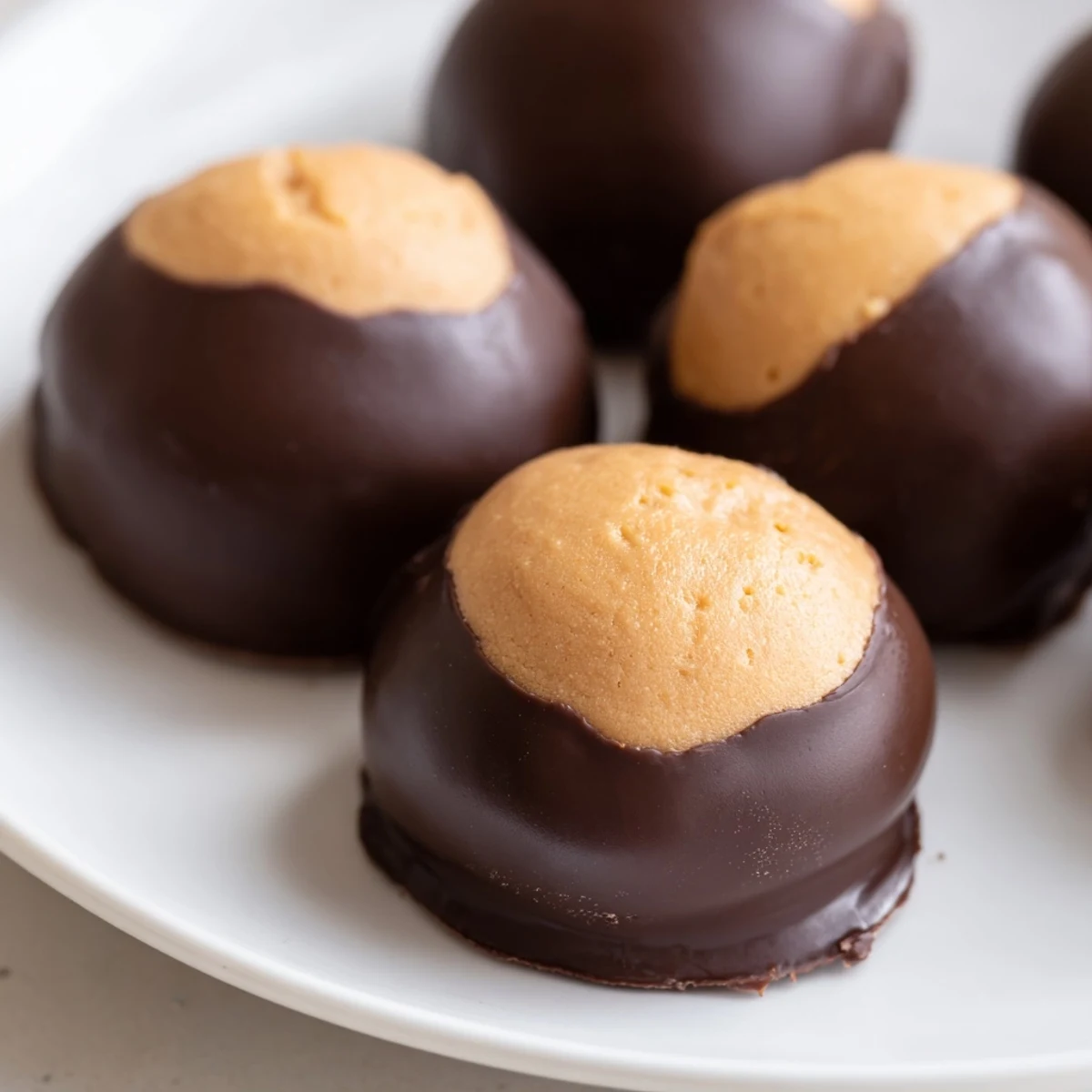 Smooth peanut butter balls partially coated in melted chocolate for classic buckeye cookies