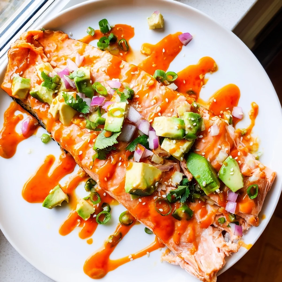 Pan-seared Bang Bang salmon topped with creamy Sriracha sauce over cool avocado cucumber salsa