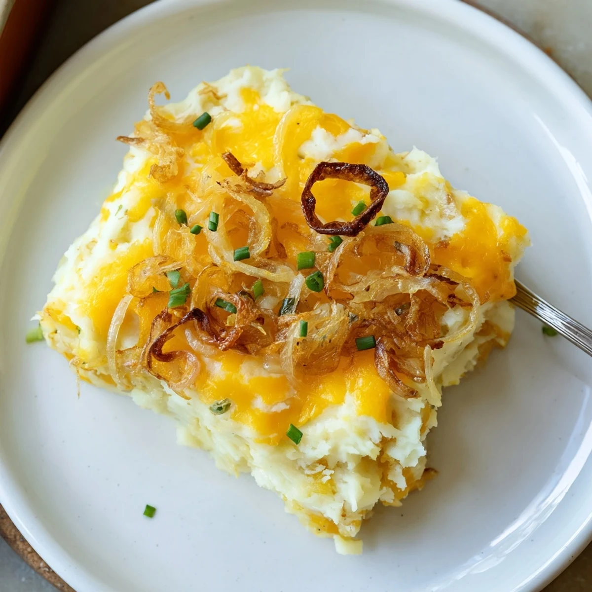 Spoonful of cheesy onion mashed potato casserole showing gooey melted cheese and caramelized onions