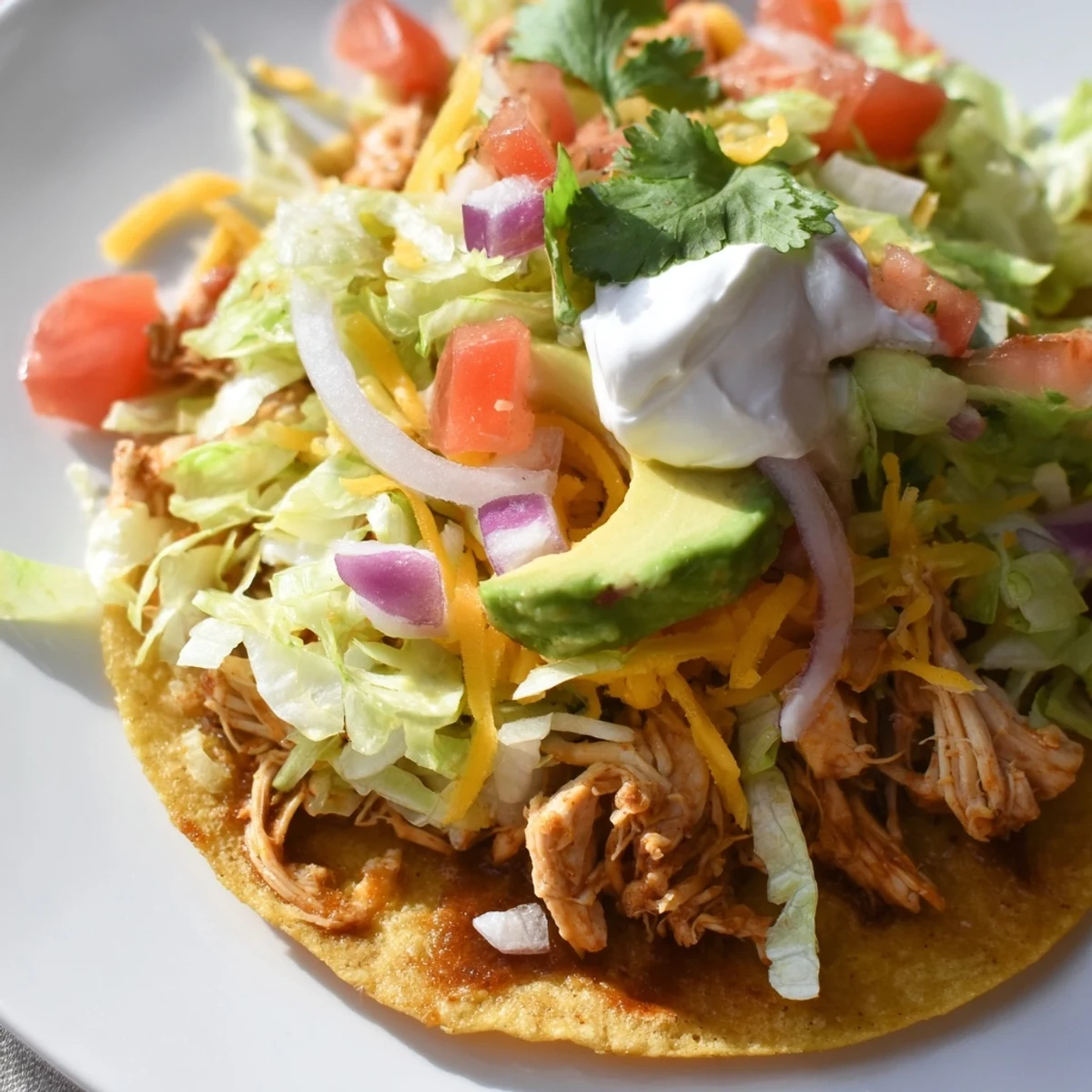Crispy Chicken Tostadas topped with fresh lettuce, cheese, and creamy avocado.  