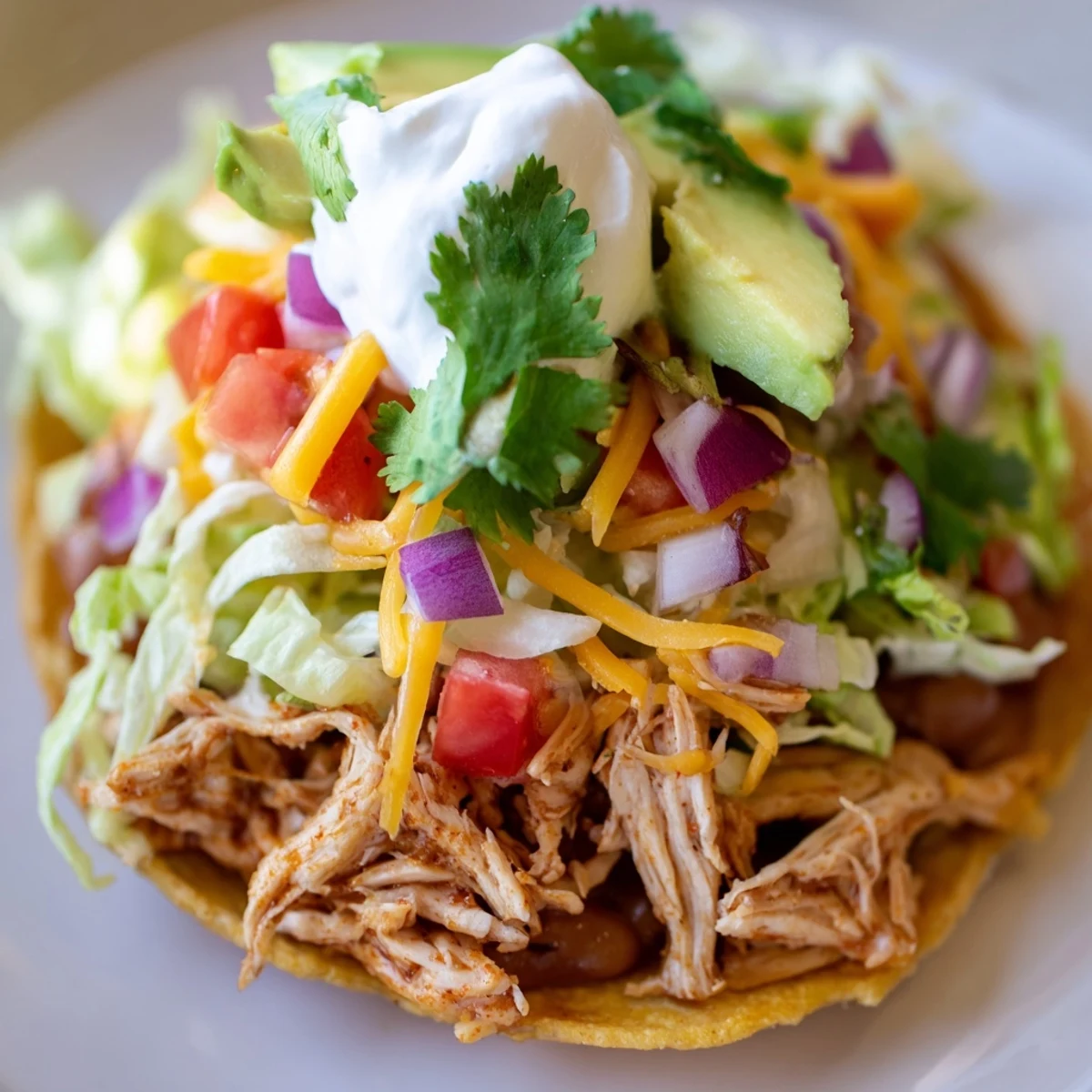 Colorful plate of chicken tostadas topped with lettuce, avocado, and sour cream