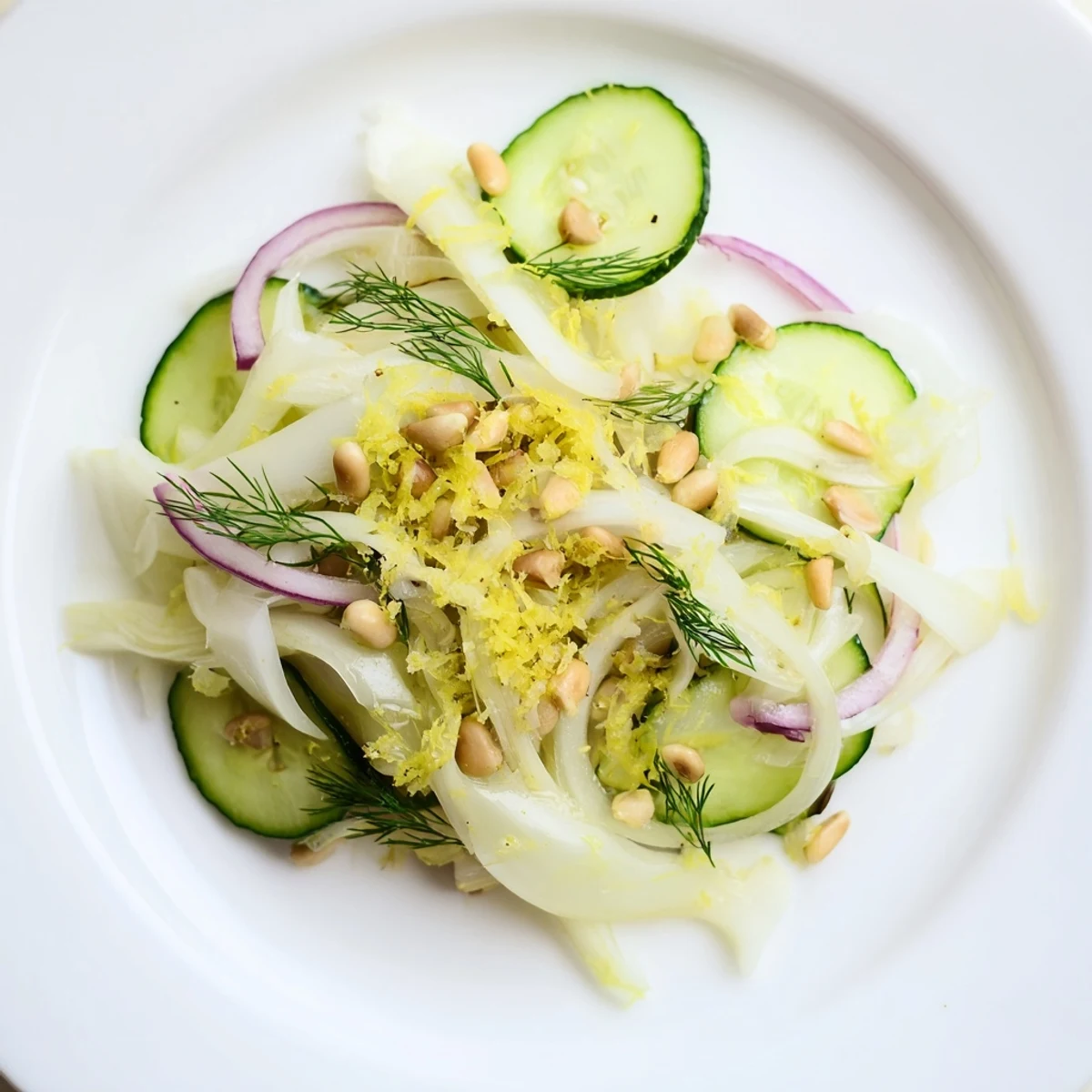 Bowl of refreshing crisp fennel cucumber salad garnished with lemon zest and pine nuts.