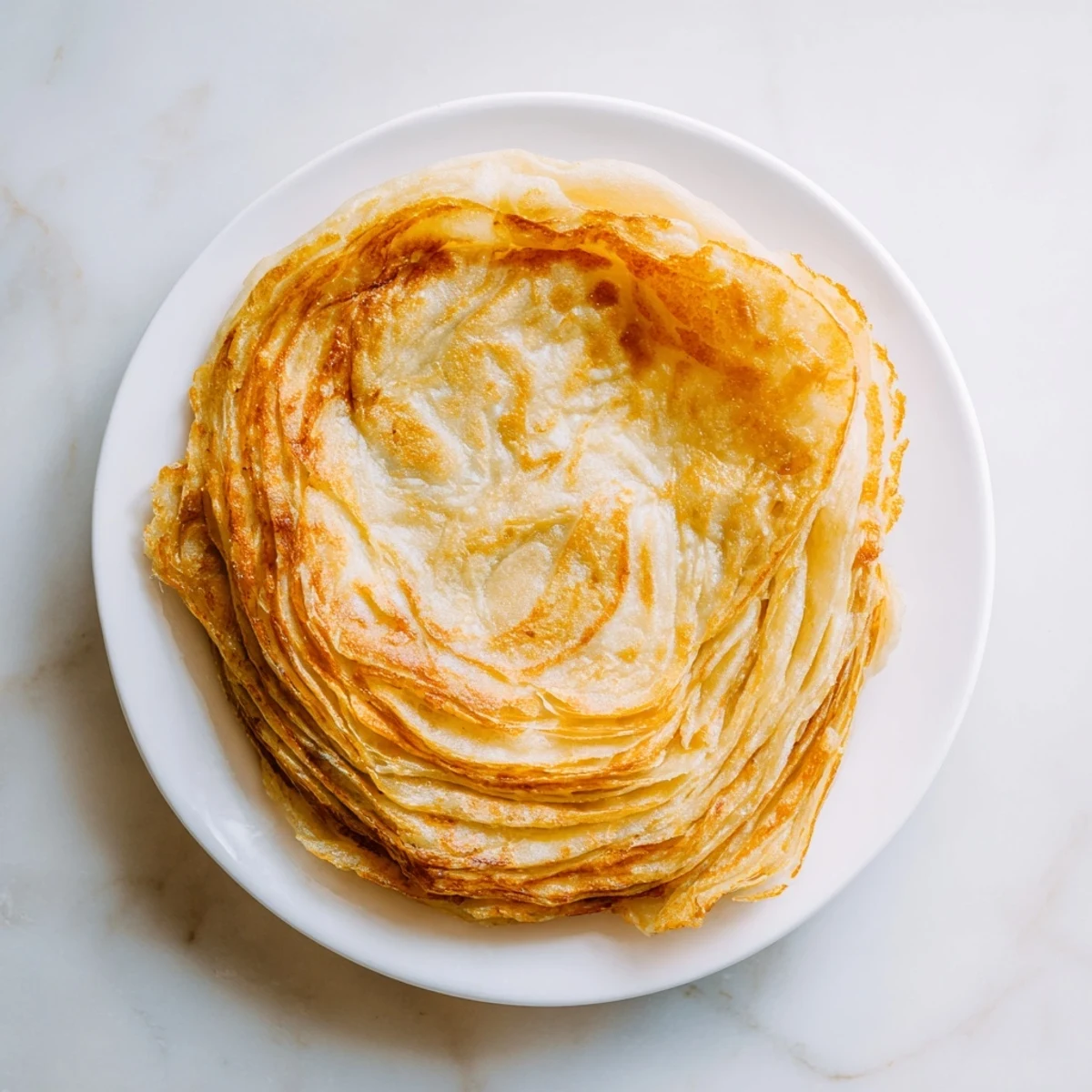 Crisp layers of buttery Roti Canai flatbread freshly cooked on a skillet.  