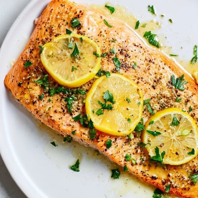 Flaky, oven-baked salmon fillets brushed with olive oil and zesty lemon pepper seasoning on a parchment-lined sheet pan.