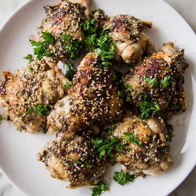 Juicy roasted Zaatar Tahini Chicken Thighs with crispy skin and sesame seeds on a baking sheet.