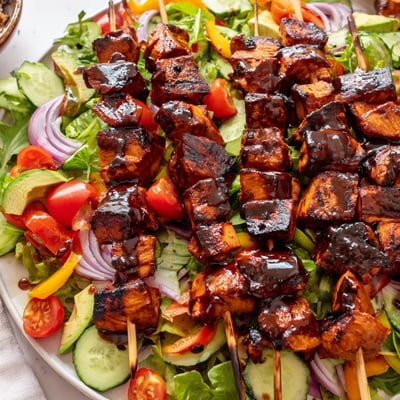 Juicy grilled BBQ chicken skewers arranged over fresh vegetables with tangy honey mustard dressing